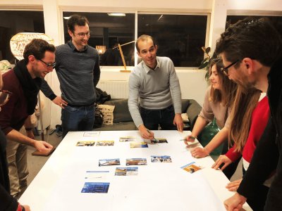 6 personnes debout autour d'une table essayant de positionner les cartes de la fresque du numérique dans le sens des causes et conséquences.