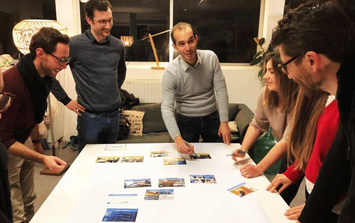 6 personnes debout autour d'une table essayant de positionner les cartes de la fresque du numérique dans le sens des causes et conséquences.